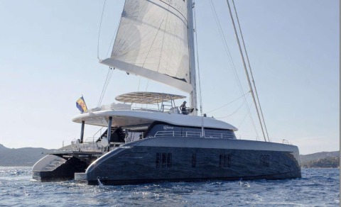 Side view of a luxury sailing yacht, person on the upper deck with sails raised, sea and horizon in the background