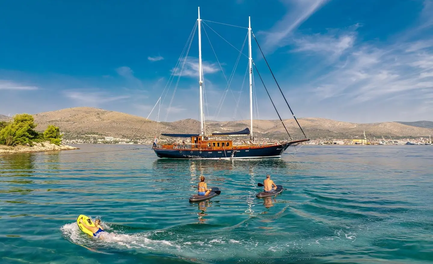 Yacht named Smart Spirit anchored near a sunny shore with people swimming nearby