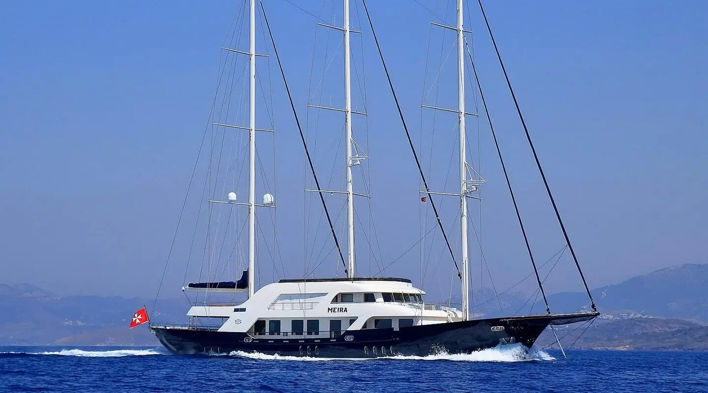 Meira yacht with white hull and tall masts anchored in blue sea