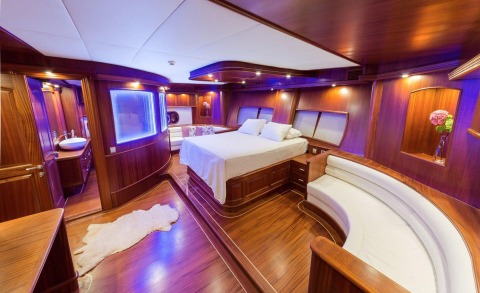 Halcon Del Mar master cabin interior with wood paneling and white bed, curved seating, and blue ambient lighting