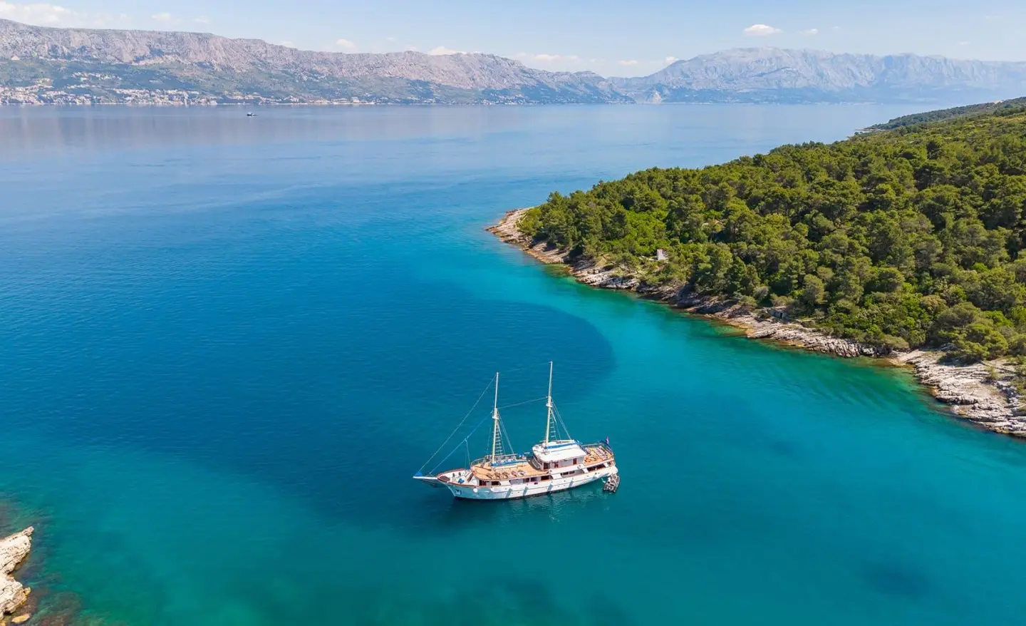 Luxury gulet Mendula anchored in turquoise bay with clear water and coastline