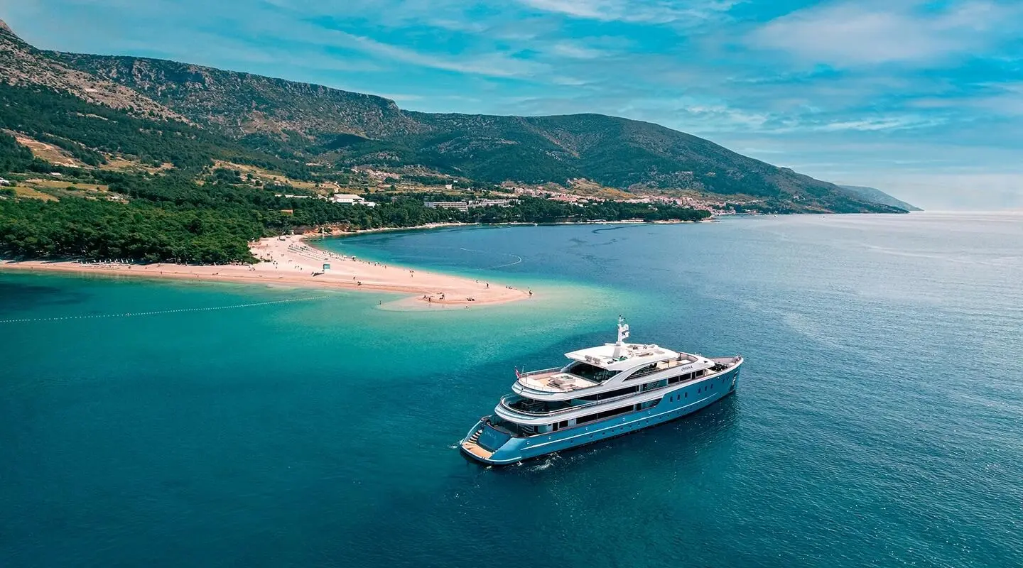 A luxurious white yacht named Ohana anchored near a sandy beach and blue-green waters