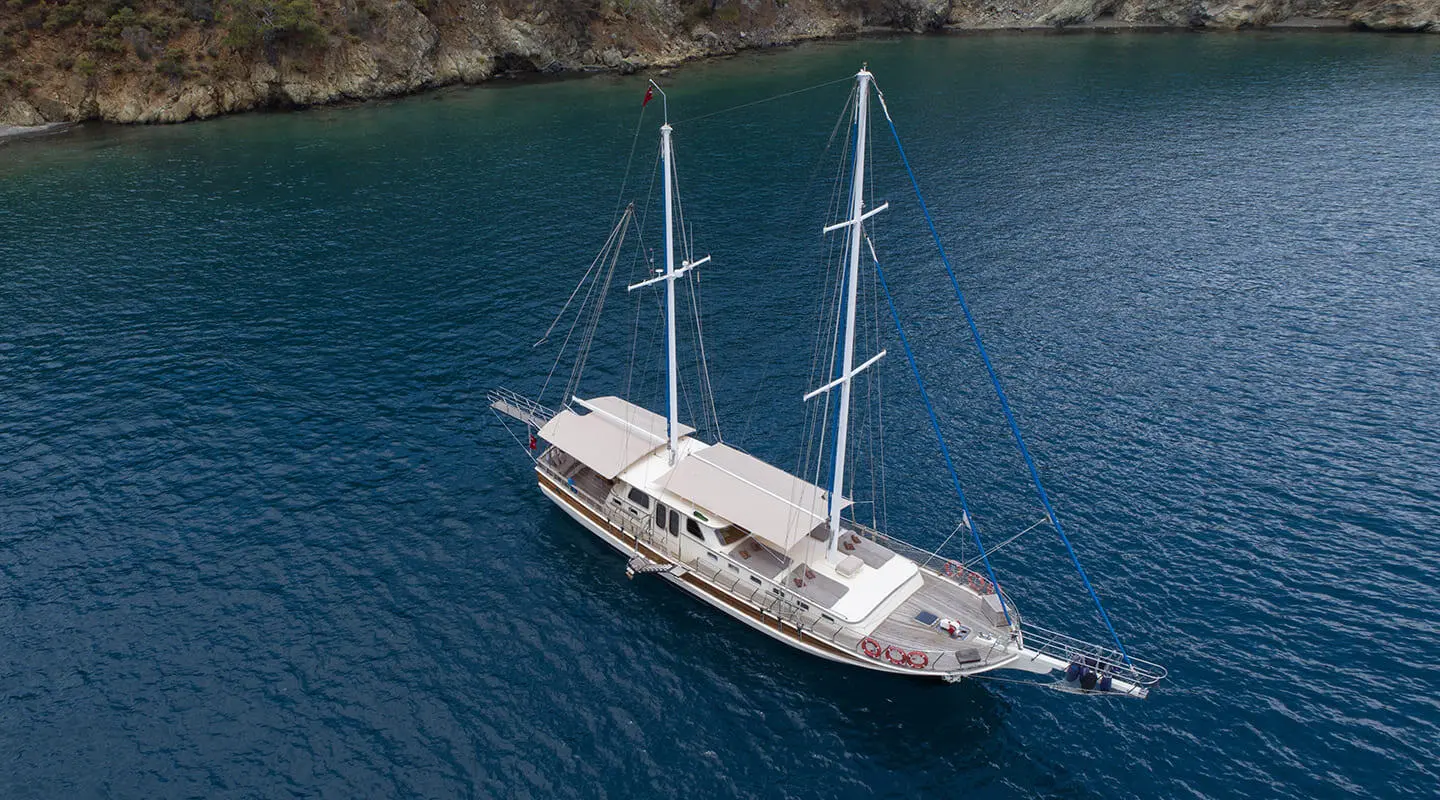 Aerial view of a white yacht named Faralya anchored in deep blue water near rocky coastline