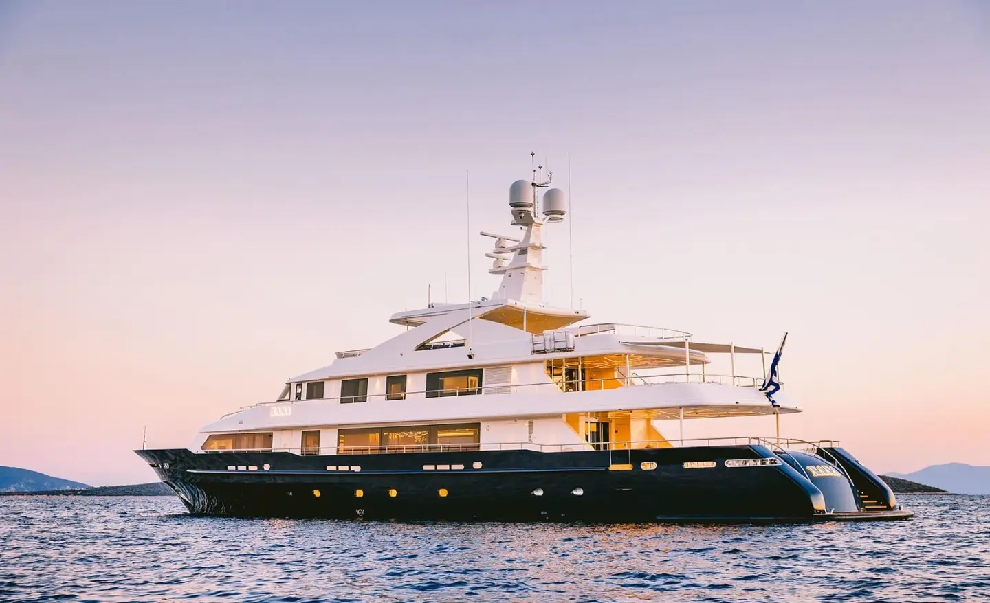 Xana yacht at sunset with white hull and multiple decks on calm water