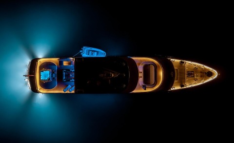 Overhead view of a luxury motor yacht at night with deck lights and blue underwater glow
