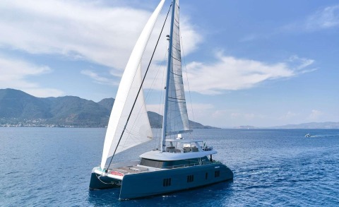 Sailing catamaran yacht with tall white sails on blue sea, side view of hull and deck