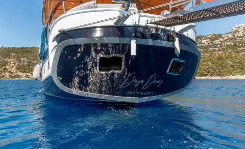Rear view of a dark blue yacht named Derya Deniz at sunset with rigging and hull reflections in calm water