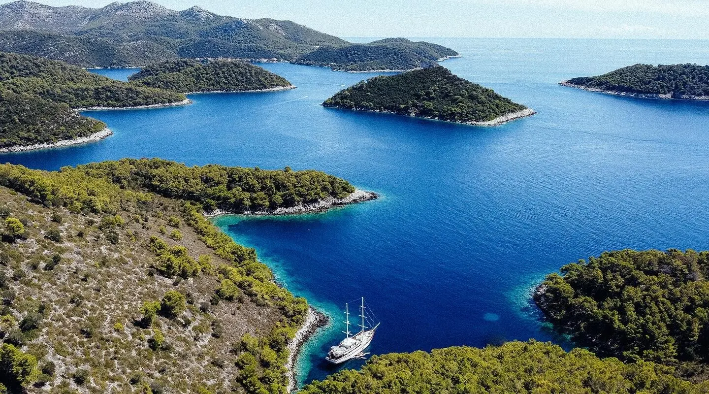 Corsario yacht anchored near blue cove with rocky coastline and islands at sunset