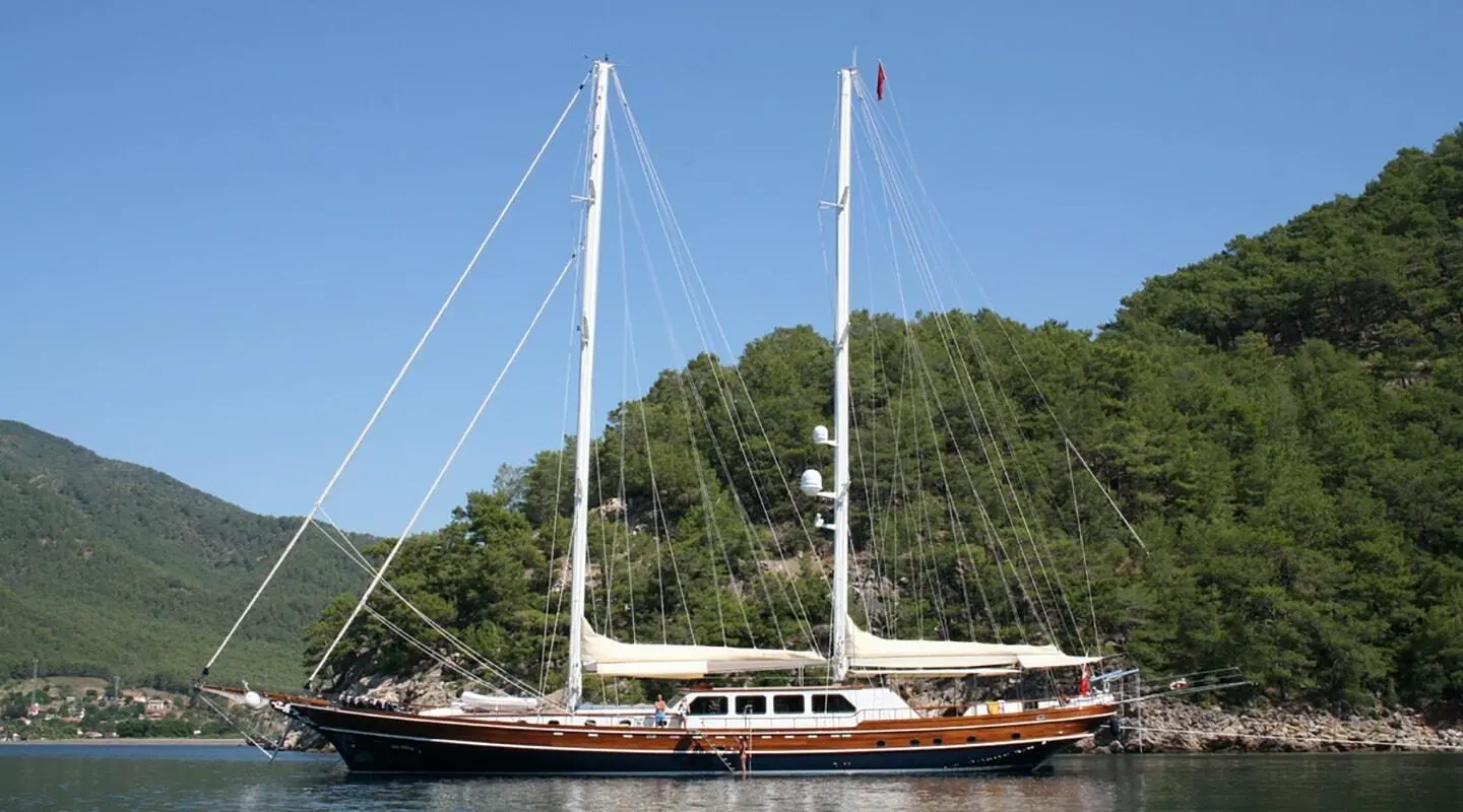 Gulet Kaya Guneri 5 anchored on calm water with forested shore backdrop