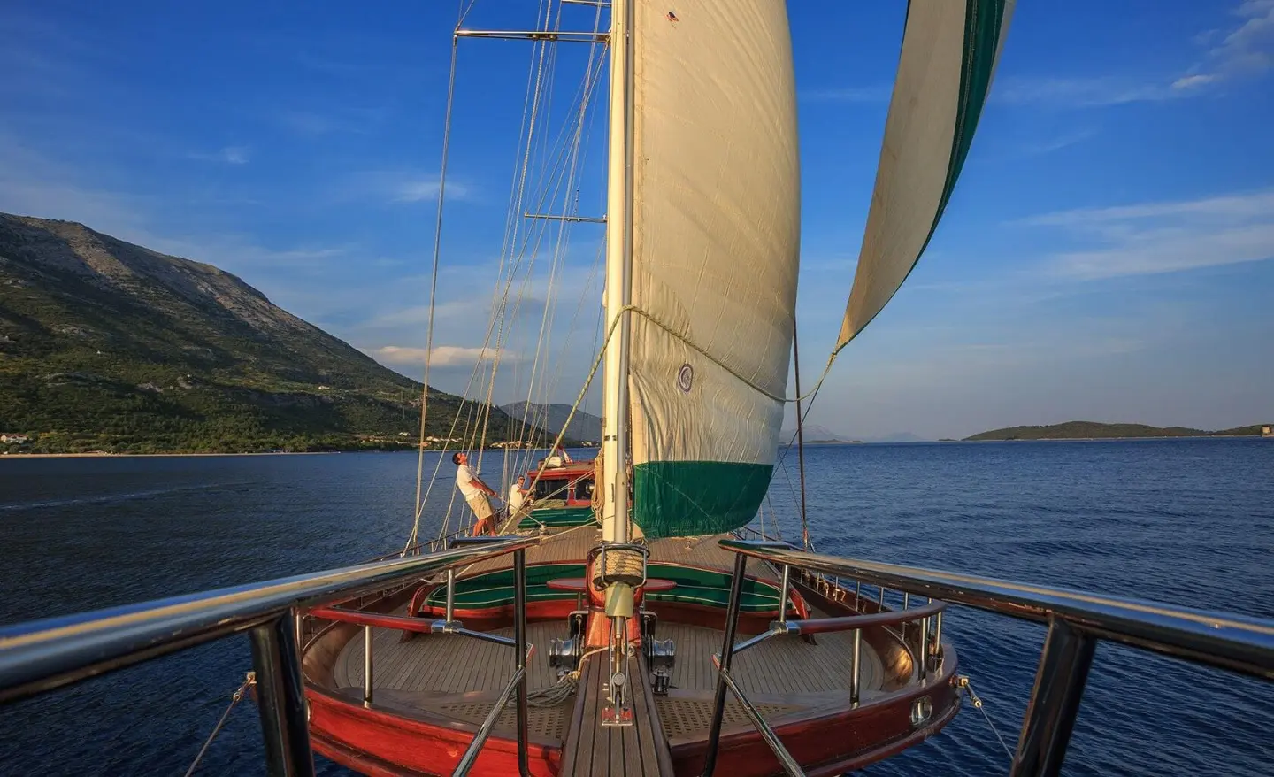 View from the deck of a sailing yacht with large sails, blue sea and distant shores