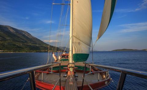 View from the deck of a sailing yacht with large sails, blue sea and distant shores