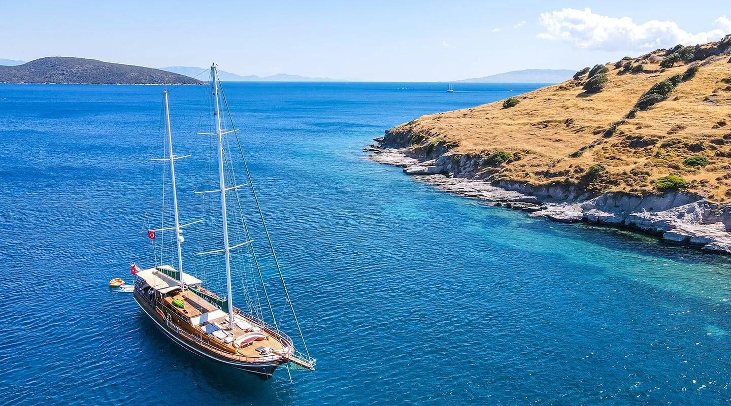 Luxurious sailing yacht anchored on calm blue sea near rocky shore