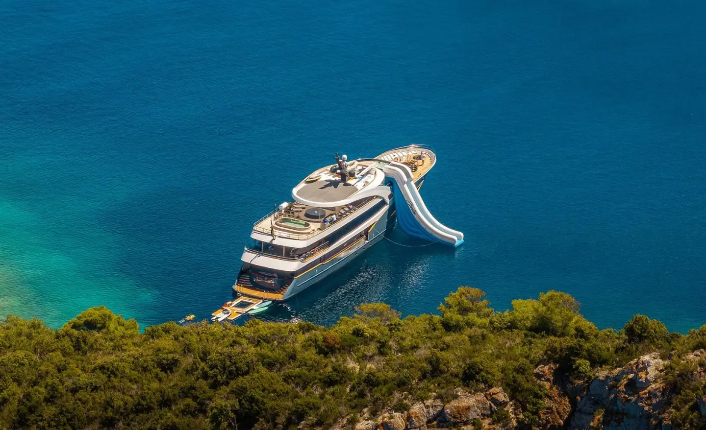A sleek luxury yacht named Bella anchored near rocky coastline on blue sea