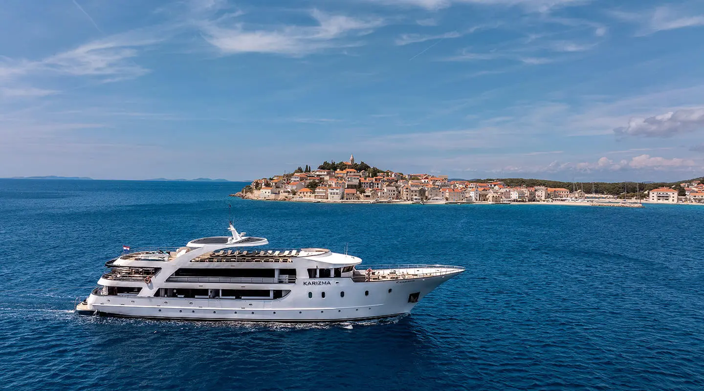 Karizma yacht sailing on blue sea, white superstructure, rocky island in distance