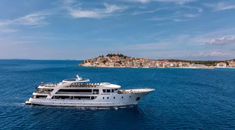 Karizma yacht sailing on blue sea, white superstructure, rocky island in distance