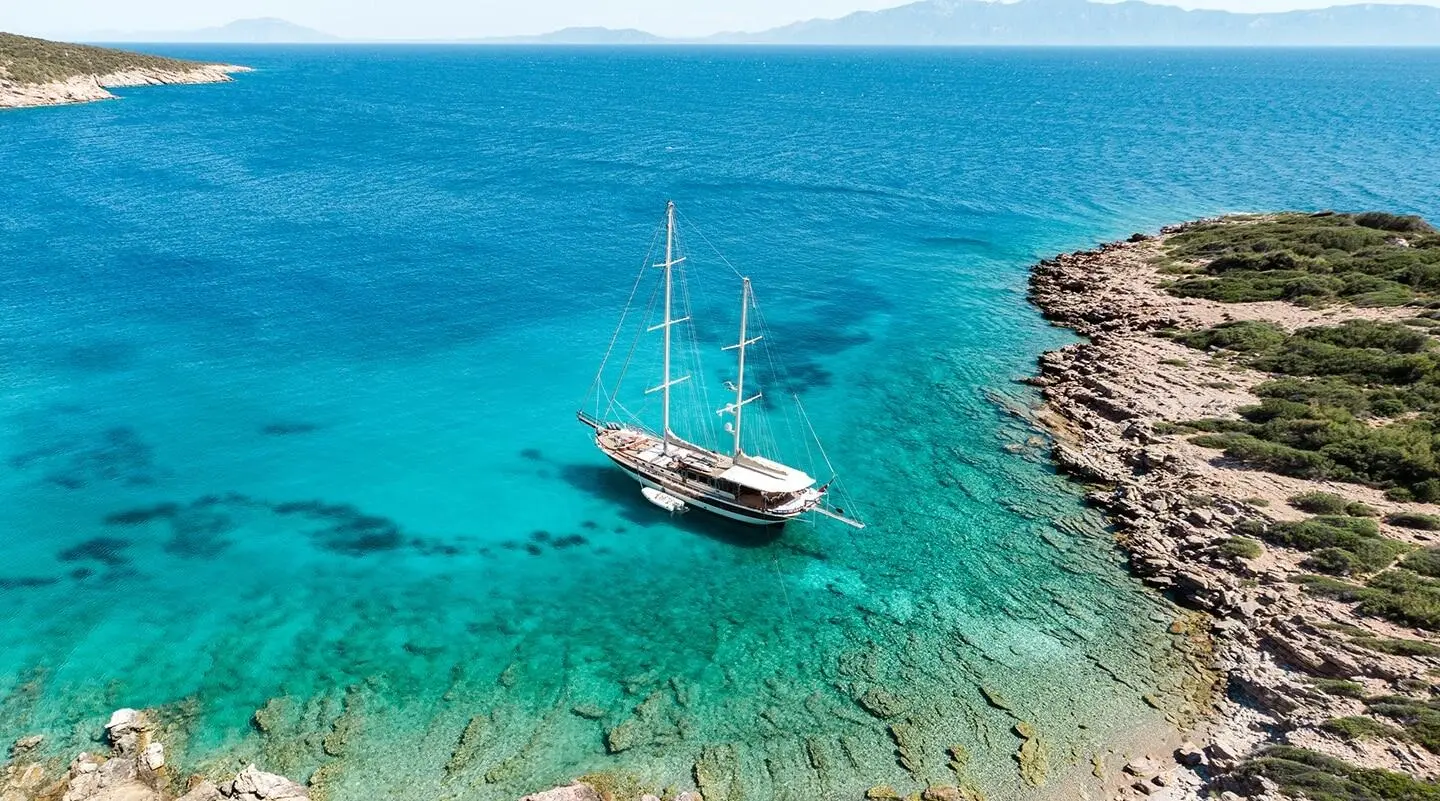 Gulet Estrella De Mar anchored in turquoise water near rocky shoreline
