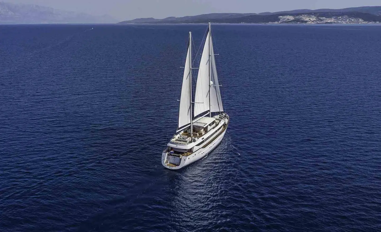 Omnia yacht sailing in blue water with white sails and small wake