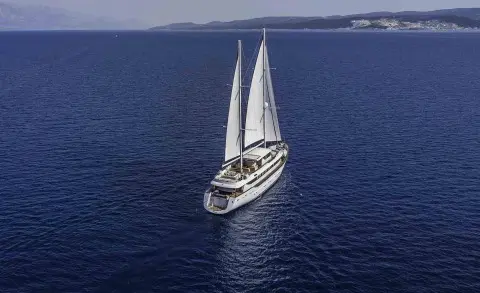 Omnia yacht sailing in blue water with white sails and small wake