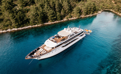 Aerial view of the white yacht Cristal anchored in clear blue water by a forested shore