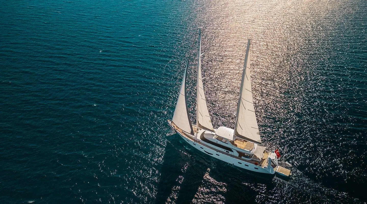 Top-down view of a white sailing yacht Angelo III anchored near blue water
