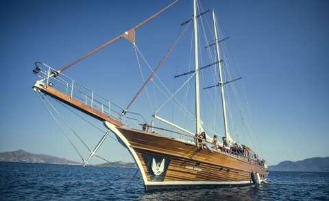 A wooden luxury sailing yacht on calm blue sea with people on deck and sails visible