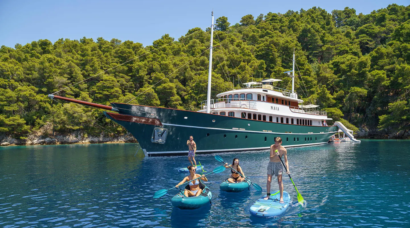 Maia motor yacht anchored near swimmers and small dinghies in clear blue water