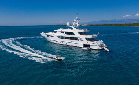 White Alalya yacht on blue water with its open deck and a jet ski nearby