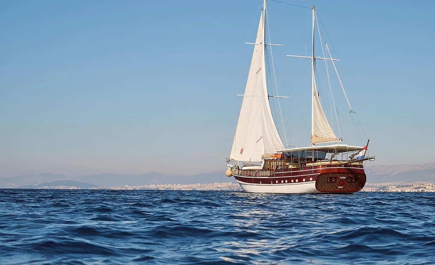 Linda yacht sailing on calm blue sea at sunset with sails up