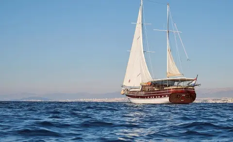 Linda yacht sailing on calm blue sea at sunset with sails up