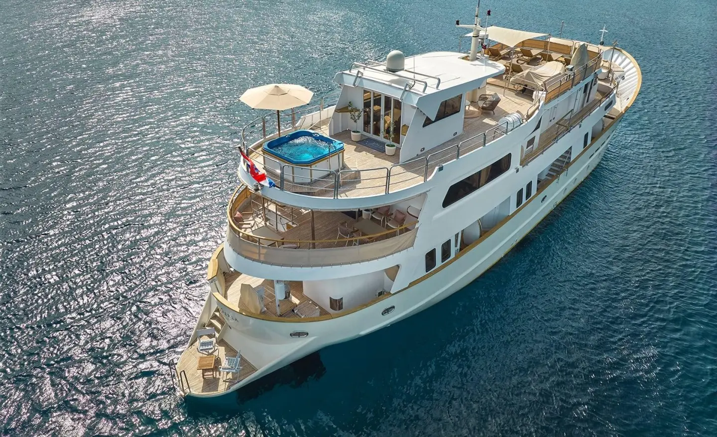 A white motor yacht named La Perla anchored in clear blue sea, aerial view