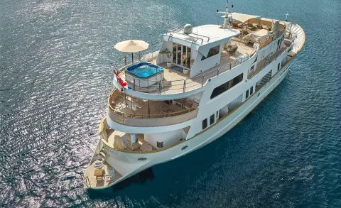 A white motor yacht named La Perla anchored in clear blue sea, aerial view