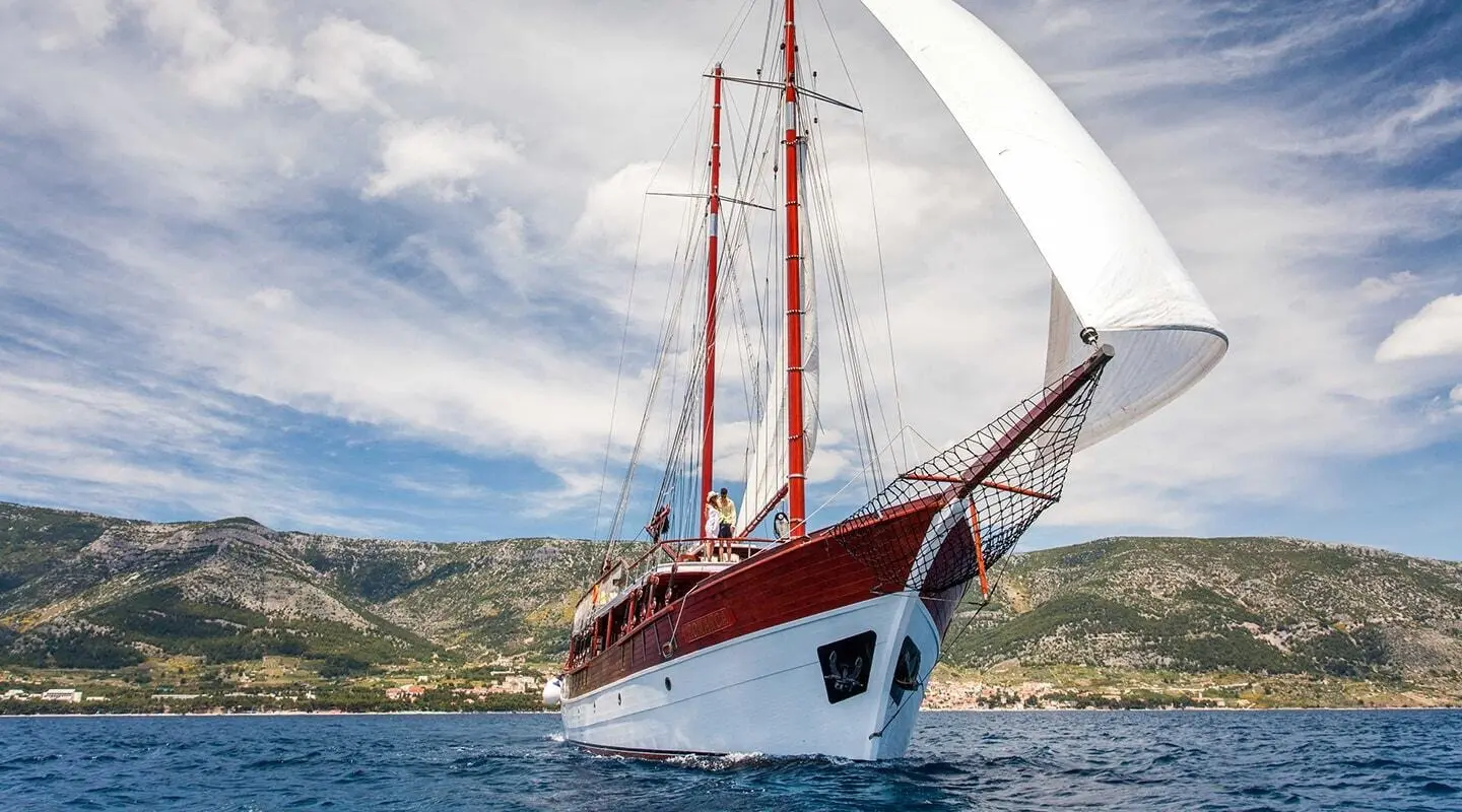 Romanca yacht sailing on blue sea with a white hull and red sails during sunset
