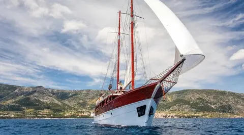 Romanca yacht sailing on blue sea with a white hull and red sails during sunset