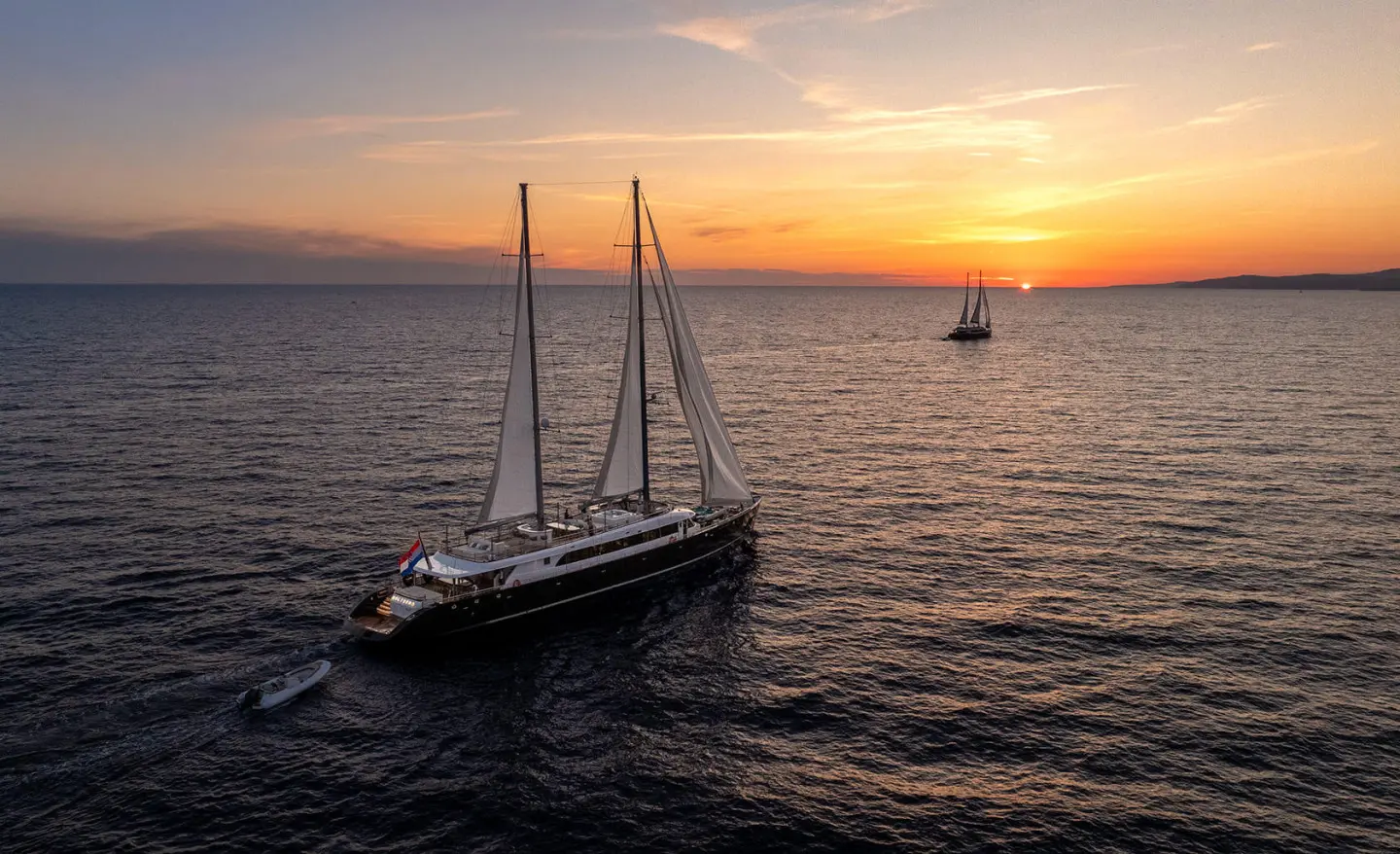 Nocturno yacht anchored on calm sea at sunset, sails down, gentle waves