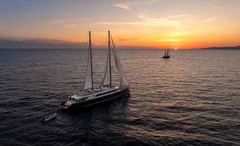Nocturno yacht anchored on calm sea at sunset, sails down, gentle waves