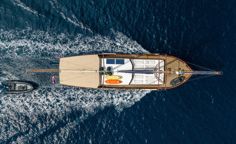 Overhead view of a luxury sailing yacht with a wooden deck moving through blue sea