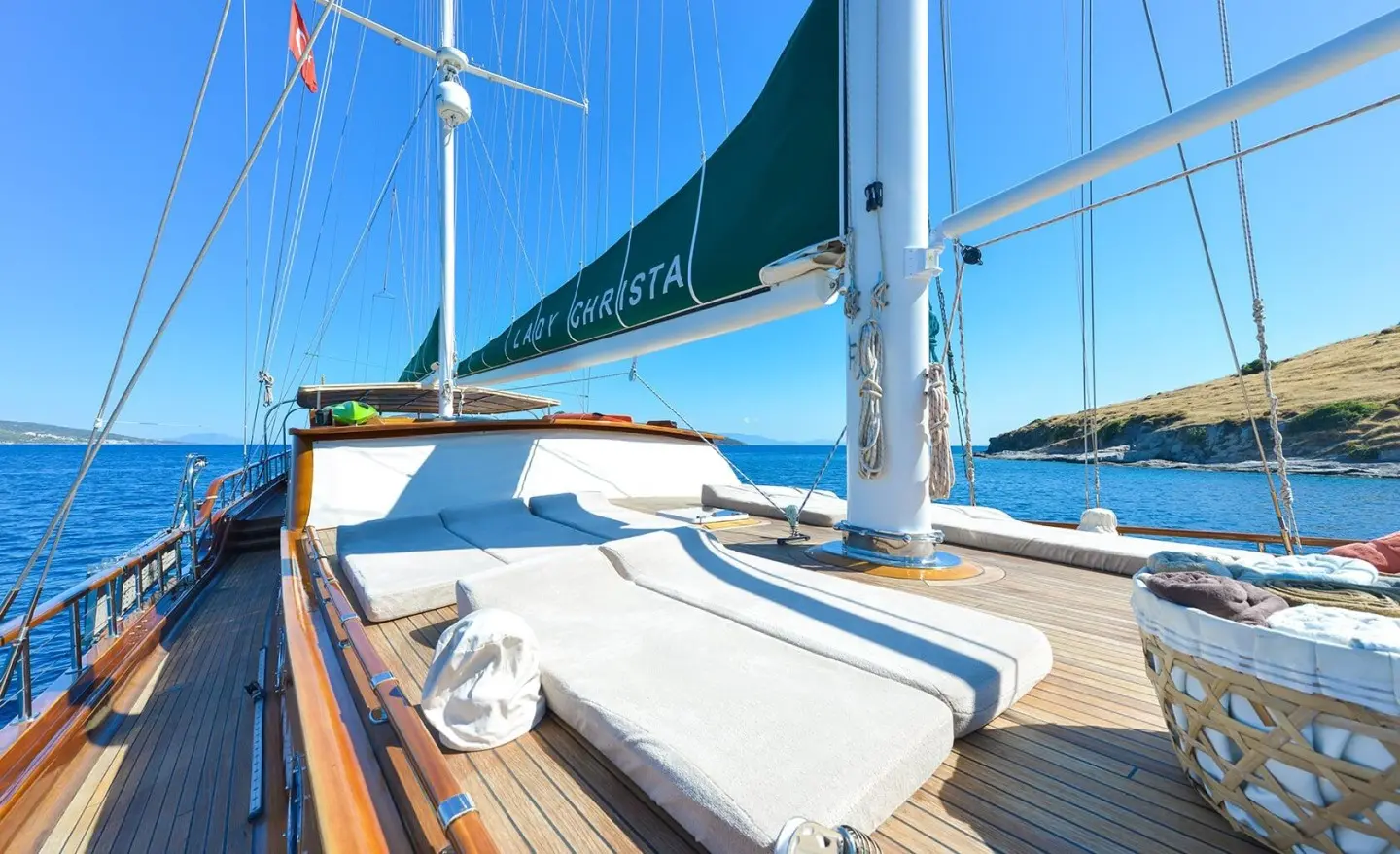 Sun loungers on deck of Lady Christa gulet with blue sails and clear sky