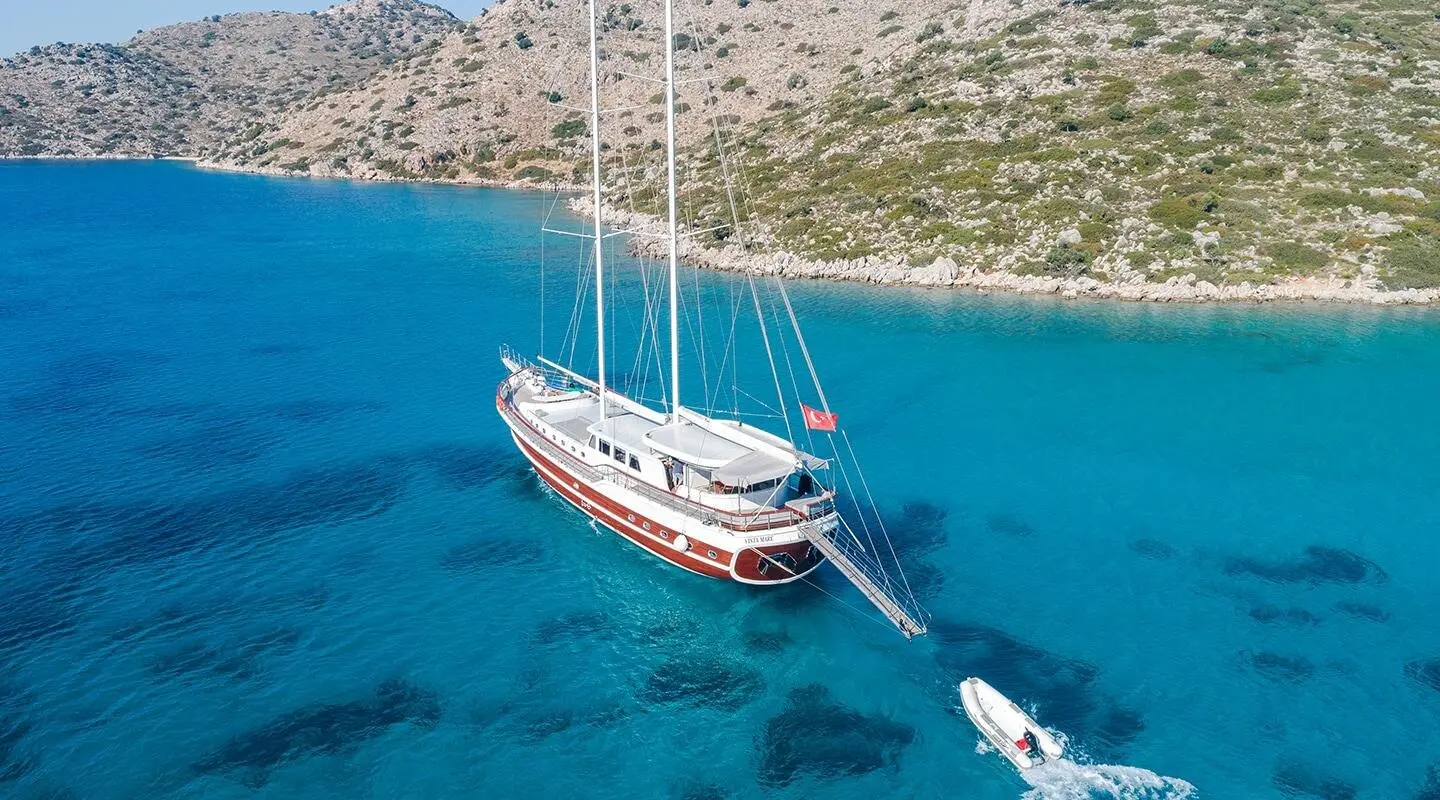 Gulet-style Vista Mare yacht anchored in clear blue water near rocky shoreline