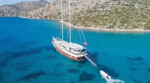 Gulet-style Vista Mare yacht anchored in clear blue water near rocky shoreline