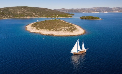Andi Star sailing near rocky island with clear blue sea, white sails up
