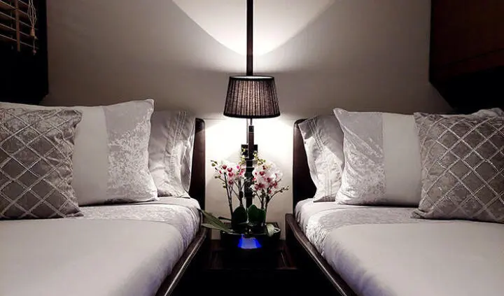 Two single beds with white linens and a bedside lamp between them aboard Miraval yacht cabin