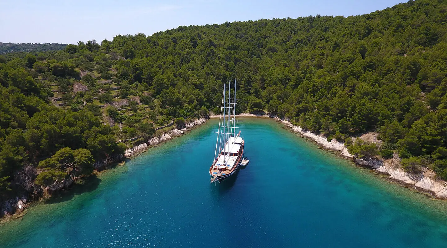 Dolce Vita yacht anchored in clear turquoise water near a forested shoreline