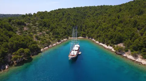 Dolce Vita yacht anchored in clear turquoise water near a forested shoreline