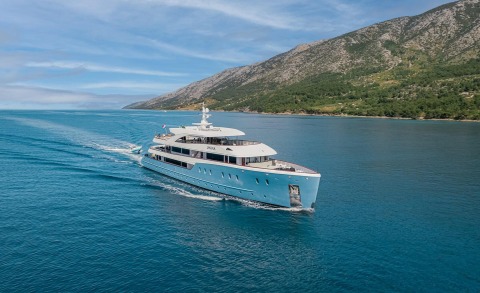 Ohana luxury motor yacht cruising along turquoise coast, blue sea, coastal mountains in background
