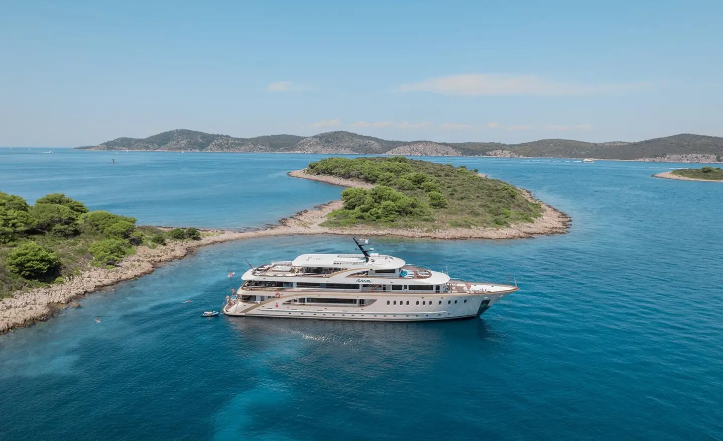 Riva motor yacht anchored in turquoise sea near small green island shore