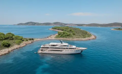 Riva motor yacht anchored in turquoise sea near small green island shore