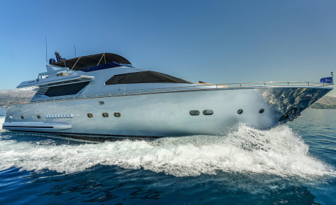 Silver motor yacht sailing at speed with side profile and forward deck, splashes creating foam in the water