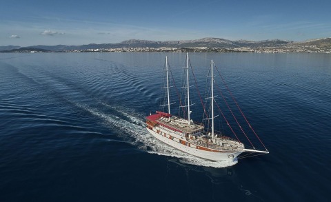 Amorena, a 44m luxury sailing yacht, glides through calm blue waters with a coastal town in the distance