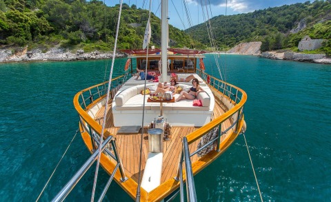 Altair yacht on the open deck with sunbathing people and turquoise sea against rocky shoreline