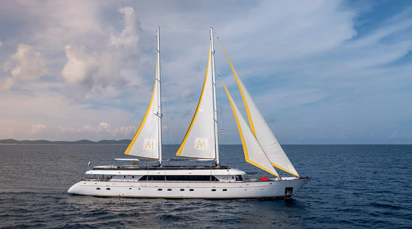 White yacht Anima Maris with two masts sailing on calm sea at sunset